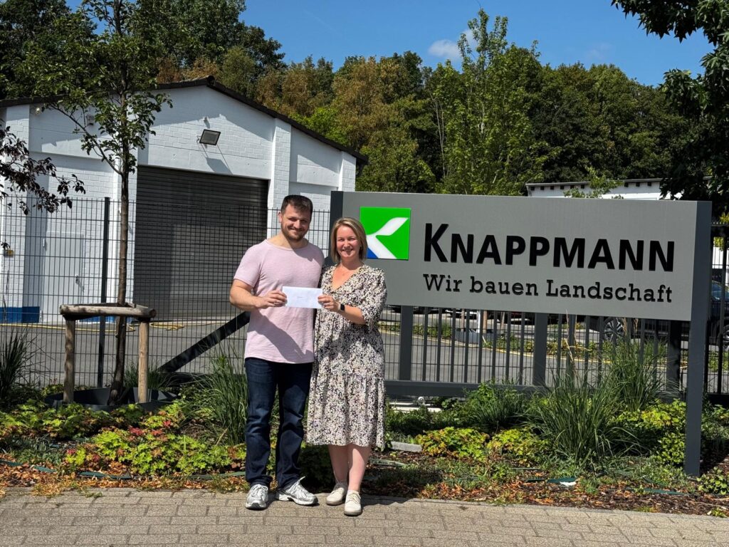 Laura Knappmann übergibt Durim Vladi einen Umschlag zur bestandenen Prüfung.
