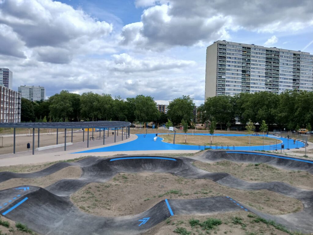 Pumptrack im Stadtpark Hochheide in Duisburg. Im Hintergrund Hochhäuser des Stadtteils.