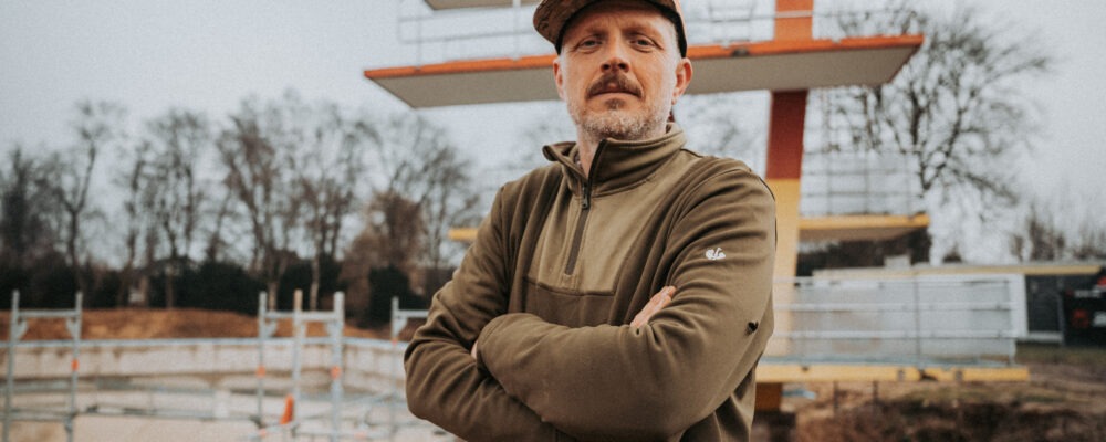 Baustellenleiter mit verschränkten Armen vor seiner Baustelle.