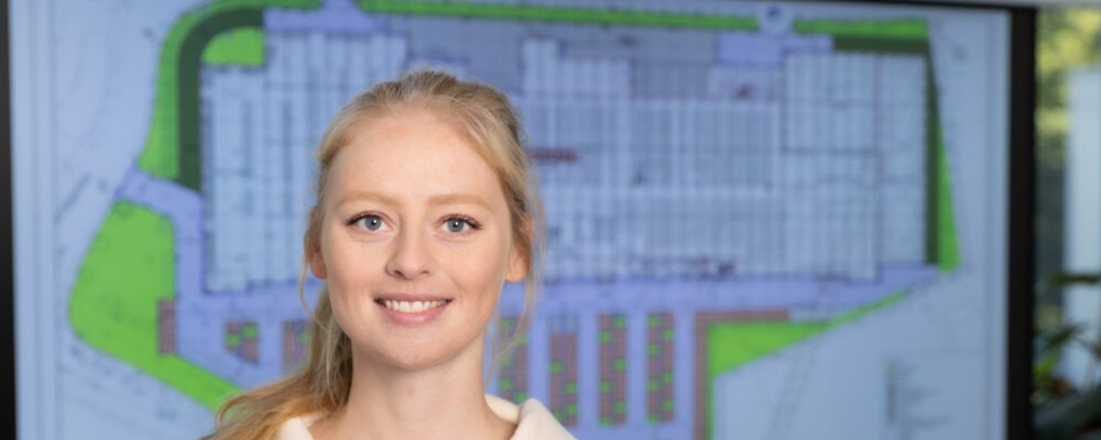 Frau steht vor einem Bauplan und lächelt