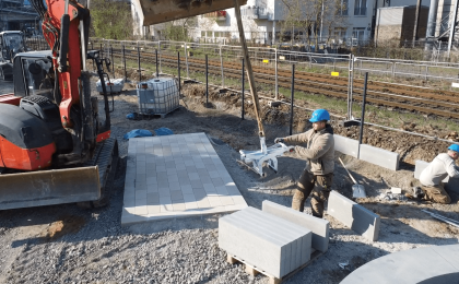 KNAPPMANN Mitarbeiter beim Setzen von Betonblöcken mit Unterstützung eines Baggers beim Projekt Quartierspark an der Glashüttenstraße in Köln-Porz.